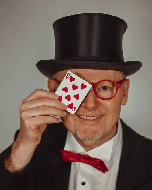 Zauberer Peter Lissek mit Zylinder, roter Brille und Spielkarte